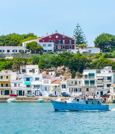 Blue fishing boat in a harbor with colorful waterfront houses in Menorca, Spain