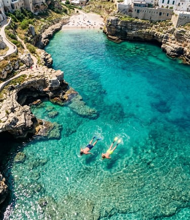 Overhead drone view of two snorkelers in turquoise water near Polignano a Mare rocky coast