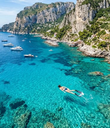 Person snorkeling in crystal clear turquoise water near Capri limestone cliffs aerial view