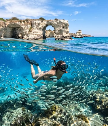 Snorkeler exploring fish school underwater near Sant'Andrea limestone arch on Salento coast, Italy