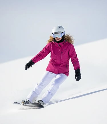 Woman in a pink ski jacket skiing down a slope on a sunny day in Grindelwald.