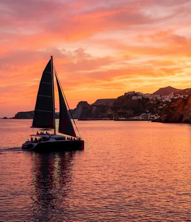 Premium catamaran sailing back to Milos harbor under vibrant orange sunset sky