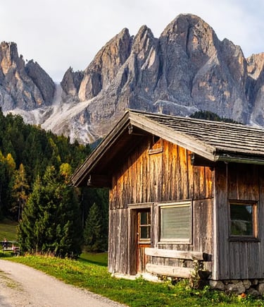 Rustic alpine cabin glowing in golden light with dramatic Dolomite peaks behind
