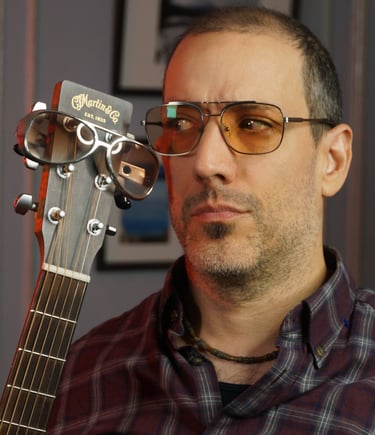 Closeup of Rob wearing aviator tinted glasses, looking at the headstock of his guitar, also sporting