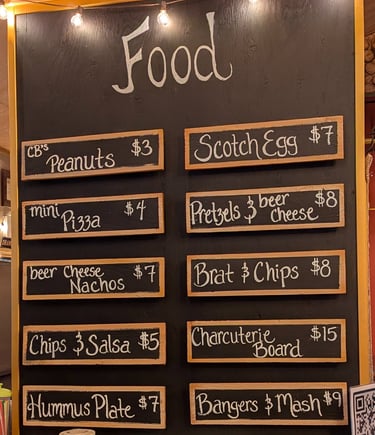 Chalkboard pub food menu listing items like scotch eggs, beer cheese nachos, and bangers and mash with prices.