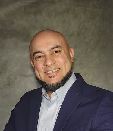 Professional headshot of a smiling bald man with a beard wearing a navy blue blazer and light blue shirt.