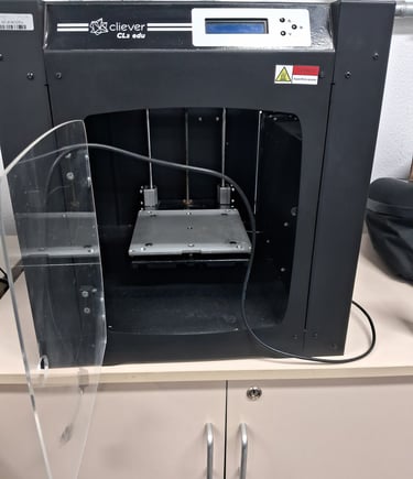 A black Cliever CL2 edu 3D printer with an open clear door sits on a white storage cabinet.
