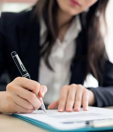 A person in business attire is writing on a business selling using a pen. The image focuses on their hands and the document.