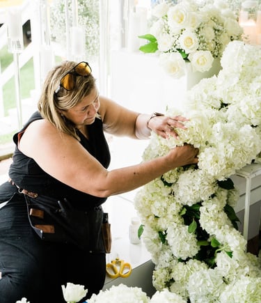 a woman in a black dress is standing in front of a large flower arrangement