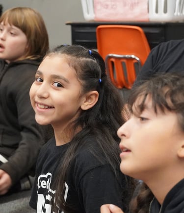 Smiling young girl participating in a group school activity with classmates in a classroom setting.
