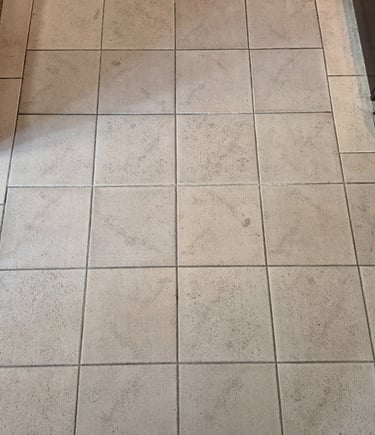 Light grey square ceramic floor tiles with dark grout installed in a kitchen area.