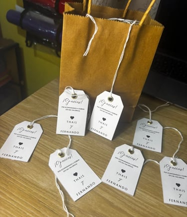 Personalized wedding favor tags with names Thais and Fernando next to a gold gift bag.
