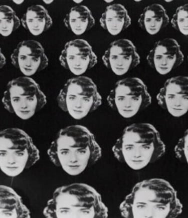 Chorus girls holding multiple large cardboard cutouts of Ruby Keeler’s face against a dark backgroun