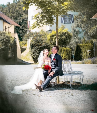 a bride and groom sitting on a bench in a park