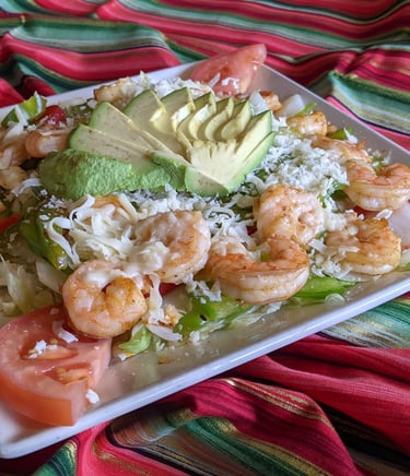 Fresh shrimp fajita salad with sliced avocado, tomatoes, and cheese on a colorful serape background.