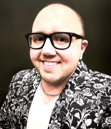 Smiling bald man wearing black thick-rimmed glasses and a floral print blazer.