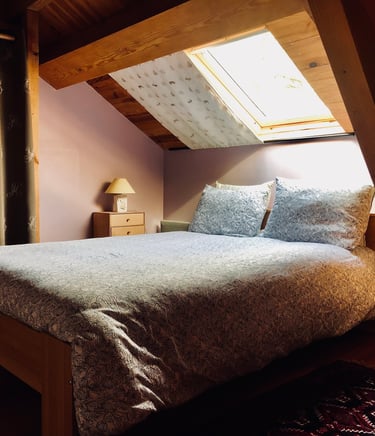 grand lit dans une chambre de la grange russell avec un velux, un rideauet une lampe de chevet