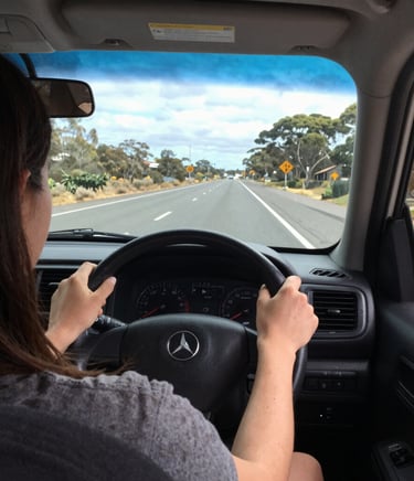 A warm, candid photo of a driving instructor calmly explaining dashboard controls to a student inside a car.
