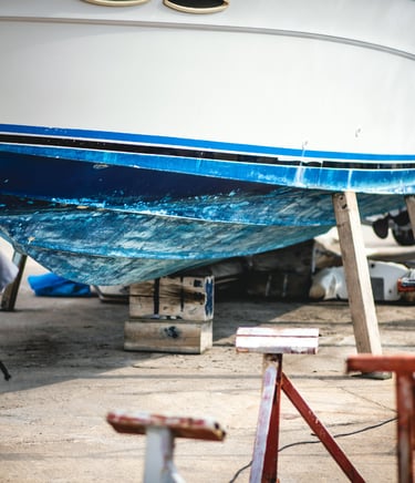 Close-up of a blue and white boat hull supported by wooden blocks for marine maintenance.