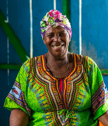 Femme souriante vêtue d'un dashiki vert vif et d'un foulard floral coloré, sur fond bleu bois.