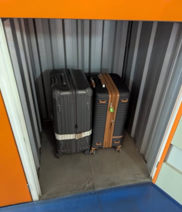 Two hardside suitcases stored inside a secure metal self-storage unit with orange trim.