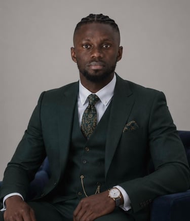 A professional man in a tailored dark green three-piece suit with a patterned tie and gold pocket watch chain.