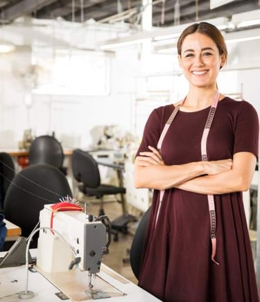 Una diseñadora de moda sonriente, con una cinta métrica en la mano, se encuentra en una fábrica de r