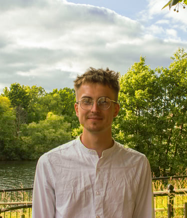 A man with glasses smiling against a river and trees as a backdrop.