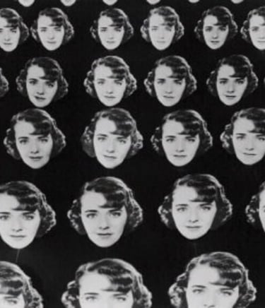 Chorus girls holding multiple large cardboard cutouts of Ruby Keeler’s face against a dark backgroun