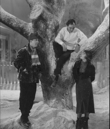 Berkeley sitting in a snowy prop tree, directing Ruby Keeler and Dick Powell on a winter set.