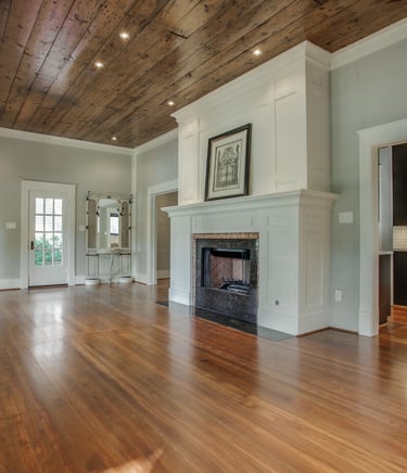 Modern living room featuring a white fireplace mantel, wood plank ceiling, and polished hardwood floors.