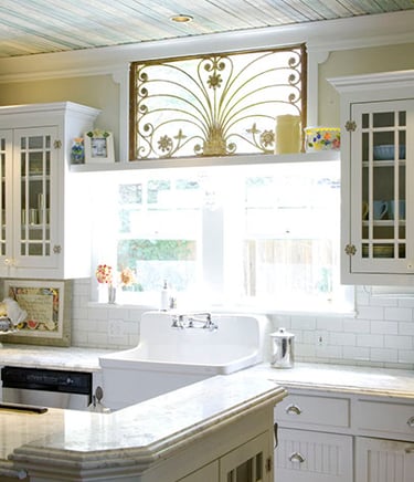 Vintage white kitchen featuring a farmhouse sink, subway tile backsplash, and ornate gold window gate.