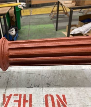 A red primed Victorian metal column and capital lying on table in industrial setting.