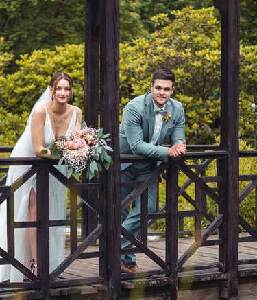 Brautpaar lehnt entspannt an einer Holzbrücke im Grünen. Hochzeitsportrait von Just Perspectives.