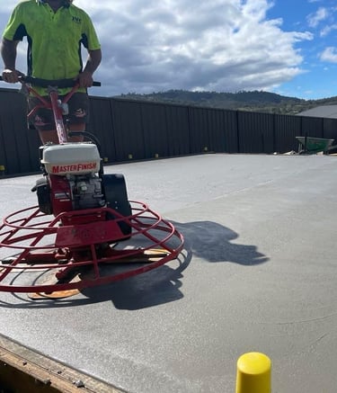 Professional concreter using a power trowel machine to finish a fresh concrete slab for a backyard patio.