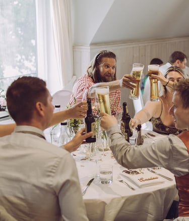 Hochzeitsgäste stoßen fröhlich mit Biergläsern am Tisch an. Authentische Eventfotografie von Just Perspectives.