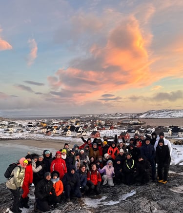 a group of people standing on a rocky cliff with a beautiful pink sky in the nordics
