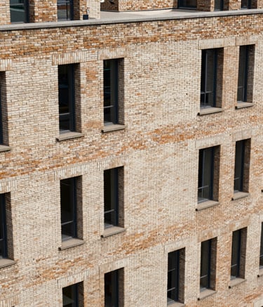 A high-angle shot of a European modern architectural building constructed with multi-toned medium tan and off-white clay bricks, showcasing exceptional craftsmanship and a robust industrial design.