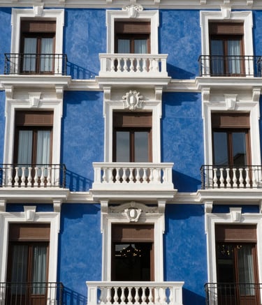 Architectural detail of a classic, high-end residential building facade in Madrid, Spain. The lighting is bright and clear, emphasizing the integrity and history of the location, with colors reflecting deep blue and white.