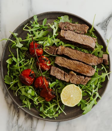 Sliced grilled steak served over fresh arugula with roasted cherry tomatoes and a lemon wedge.