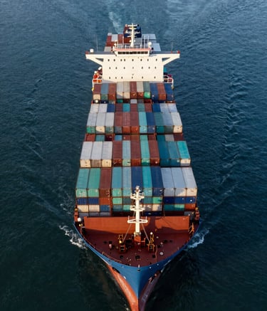 An aerial professional photograph of a massive container ship entering a modern harbor at sunrise. The water is a deep dark blue, and the stacks of white and teal containers are perfectly organized, representing global efficiency.