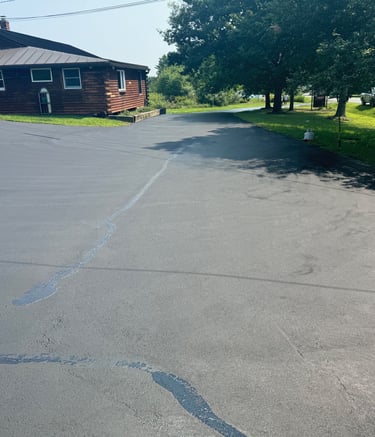 Freshly sealed asphalt driveway with crack filler next to a rustic log cabin home.