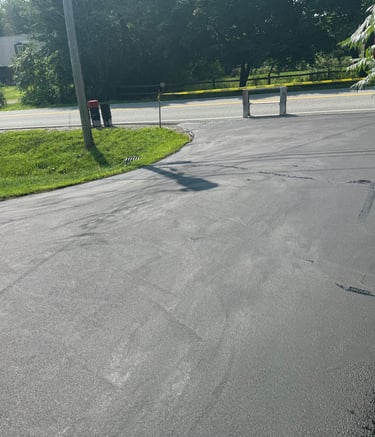 Freshly paved blacktop residential driveway leading to a rural road with yellow caution tape.