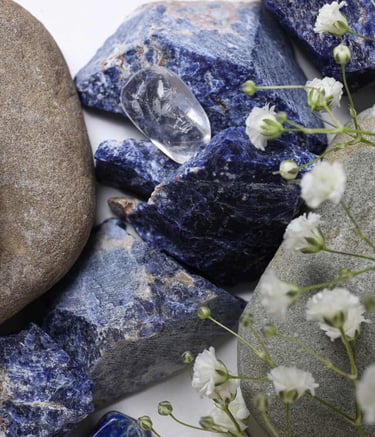 Cristales de sodalita azul en bruto y piedras de río lisas con flores blancas de paniculata