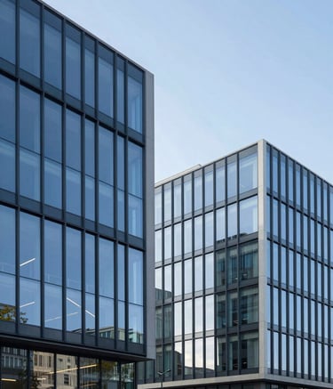 Exterior shot of a sleek, contemporary European / French office building with blue glass facades reflecting the soft blue sky. Minimalist architecture, clean lines, high-end commercial aesthetic.