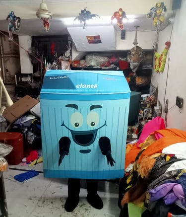A person wearing a blue Lloyd Elante washing machine mascot costume in a workshop filled with fabrics.