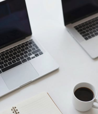 An overhead view of a clean desk with a laptop, a notebook, and a coffee cup. High contrast and professional lighting. Elements of the desk are in shades of #4E7B99 and #F5F8FA, reflecting a focused and efficient work environment.