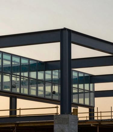 A modern construction site during the golden hour. Steel beams and concrete foundations are visible against a soft ash sky. Touches of deep slate and muted teal are reflected on structural glass surfaces.