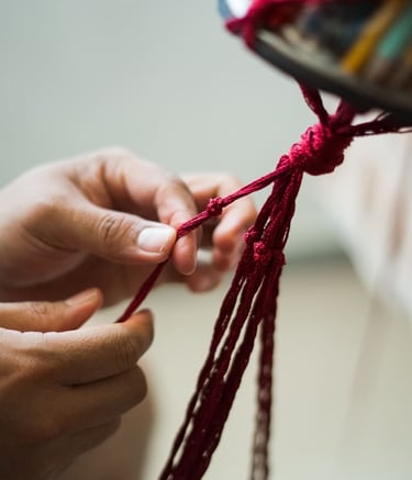 ordón rojo de macramé siendo tejido y anudado a mano para crear una pieza de arte textil