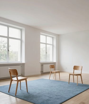 A wide, serene photograph of a modern, minimalist classroom with generous white space. Large windows let in soft light. A few wooden chairs and a soft sky blue rug create a warm, human-centered atmosphere. Professional photography, high-end interior style.
